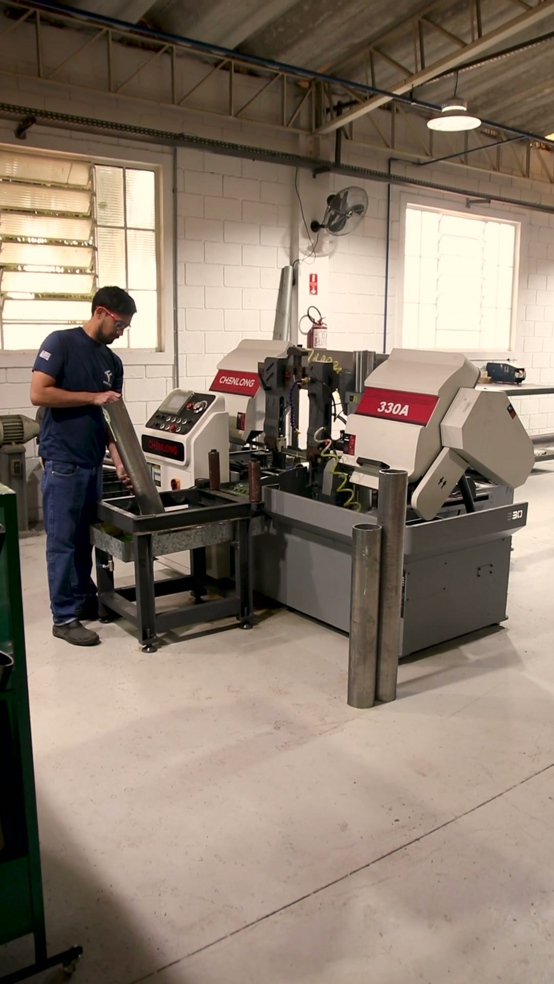 Funcionário operando a serra de corte automática, com o trilho de suporte para tubos longos, na fábrica da Forthy em Porto Feliz/SP