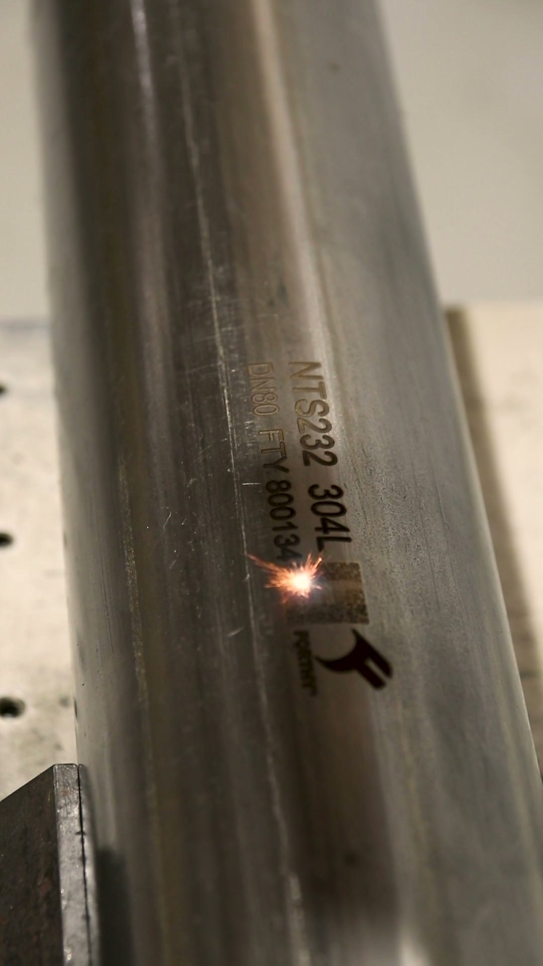 Gravadora a laser em ação, marcando o código de rastreabilidade e a norma NTS 232 num tubo de aço inox, com o logo Forthy gravado ao lado
