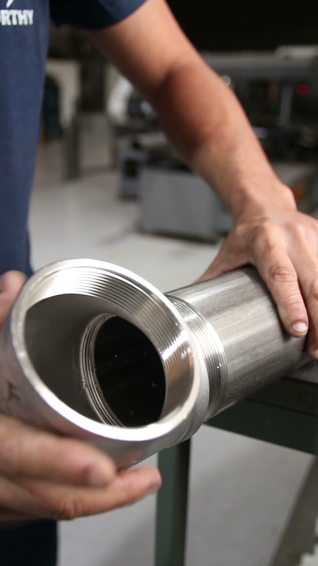 Funcionário inspecionando manualmente a rosca interna de um cotovelo de aço inox de grande diâmetro na fábrica da Forthy
